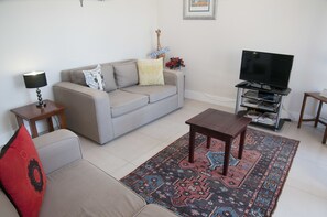 A living room with a sofa, a coffee table, a TV on a stand, a lamp, and a rug.