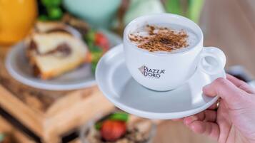 Une main tenant une tasse de café ornée d’un logo, entourée de divers aliments et d’une plante en pot.