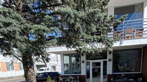Ulkoterassi, jossa on punottuja pöytiä ja tuoleja, puu ja taustalla oleva rakennus, jonka kyltissä lukee ”CITY HOTEL”.