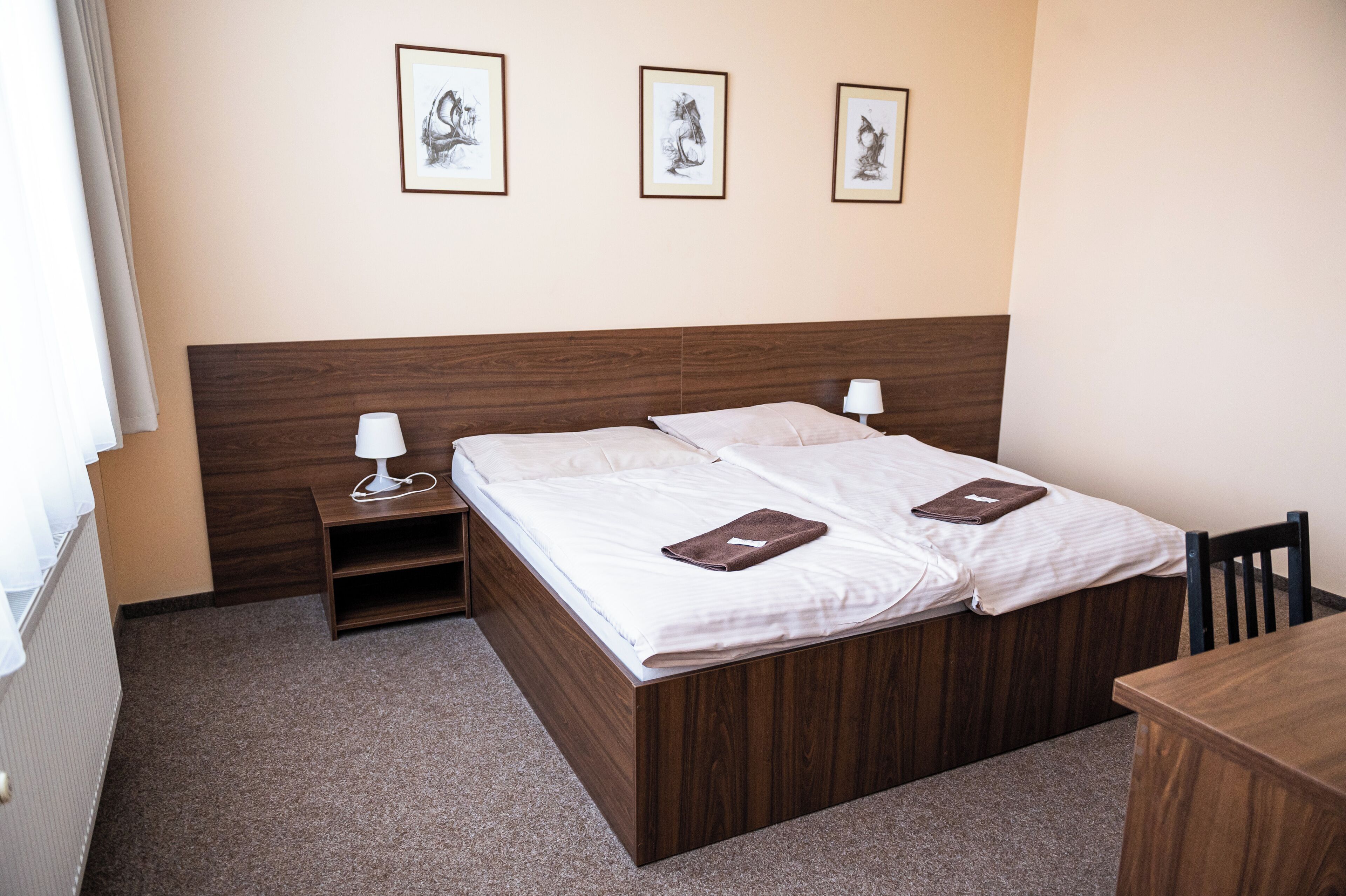Una cama doble con cabecera de madera, dos mesitas de noche con lámparas, y tres cuadros enmarcados en la pared.