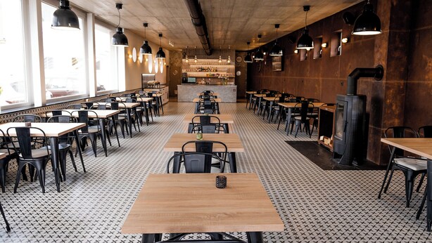 Tilava ravintola, jossa on pitkiä pöytiä ja tuoleja, baarialue sekä suuri takka.