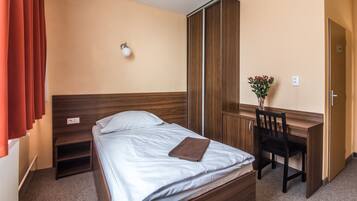 A hotel room with a bed, a desk, a chair, a nightstand, and a wall-mounted lamp.