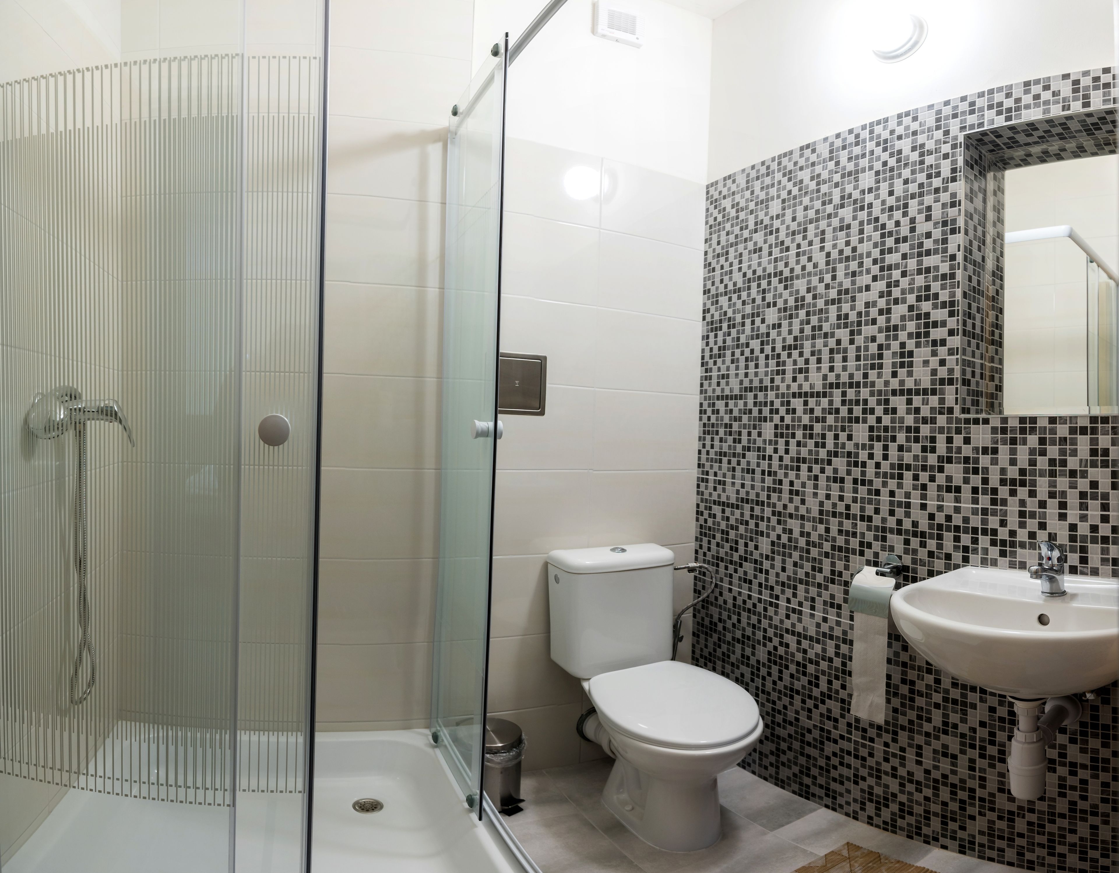 Een moderne badkamer met een douchecabine van glas, een toilet en een wastafel met een betegelde spatwand.