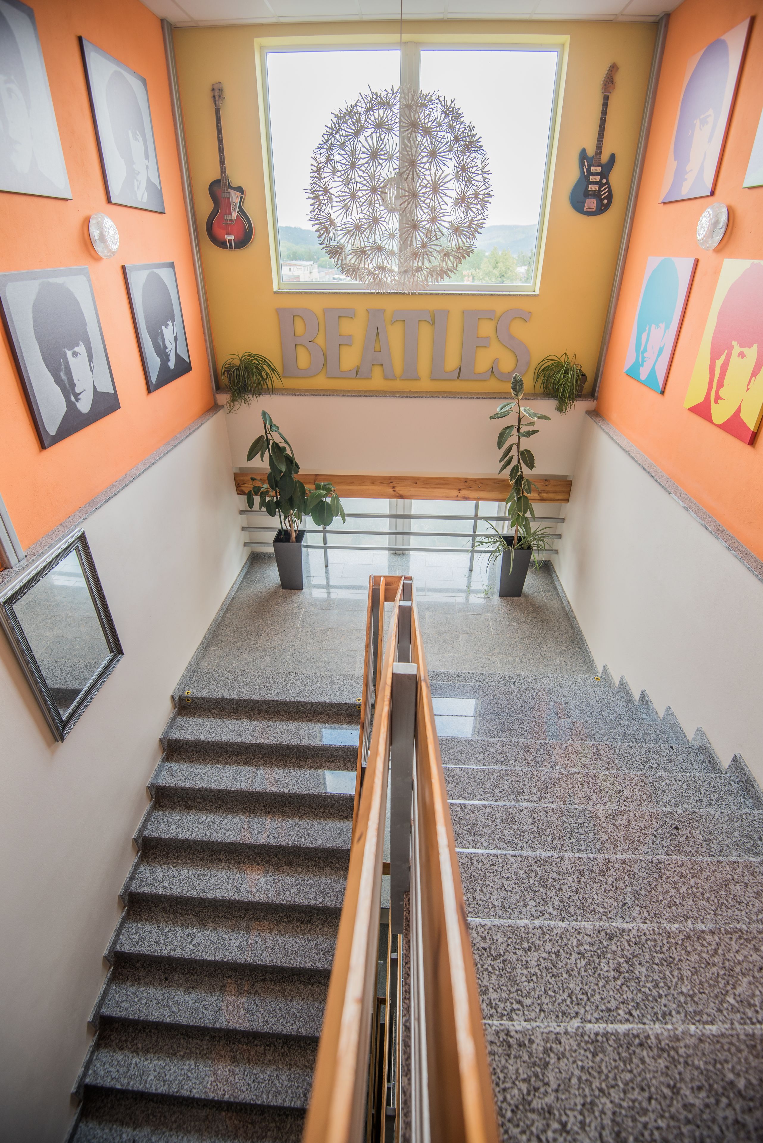 Una escalera con barandilla, plantas en macetas y una pared con cuadros y un letrero que dice 'BEATLES'.
