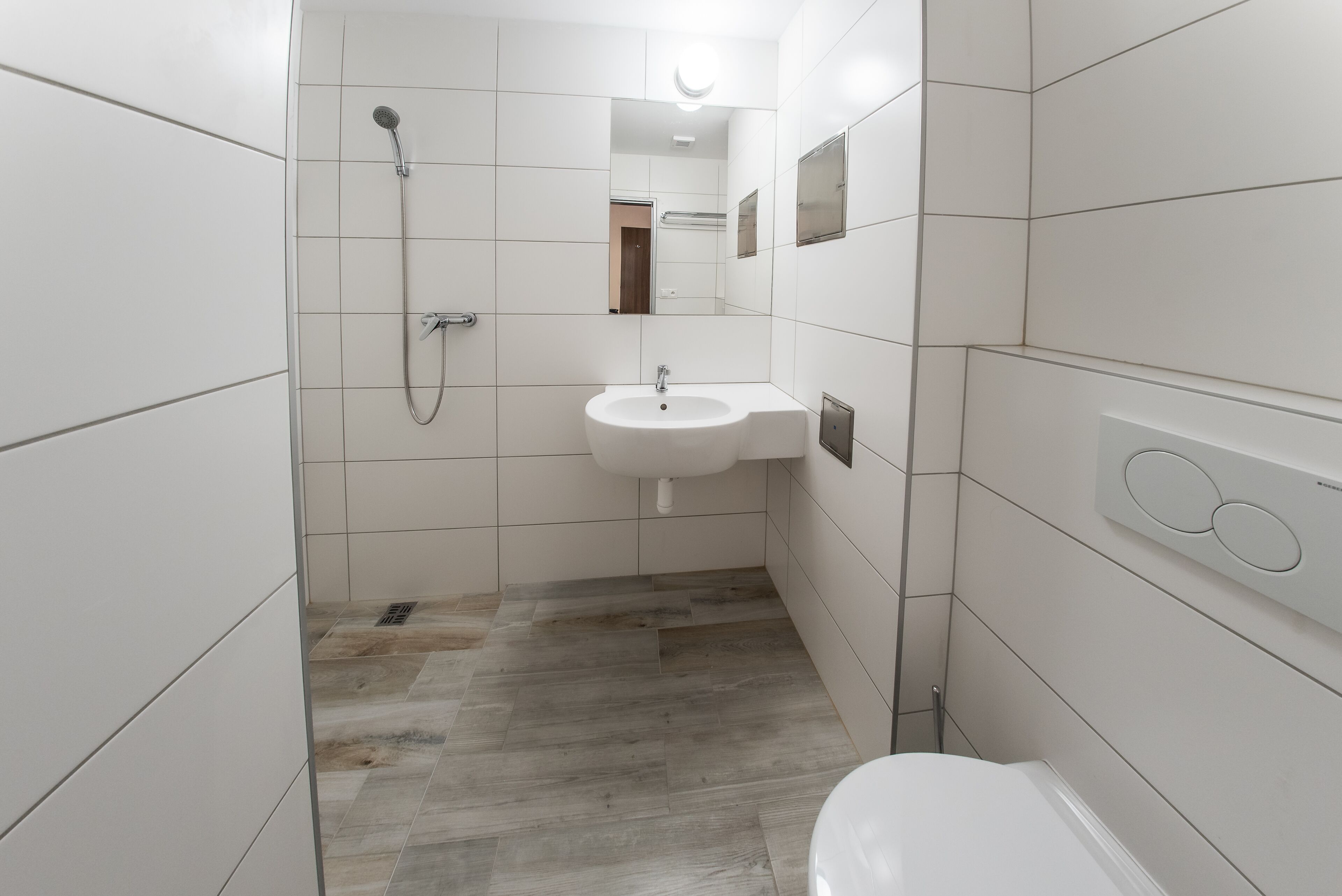 Un baño moderno con azulejos blancos, un lavabo, una ducha e inodoro.