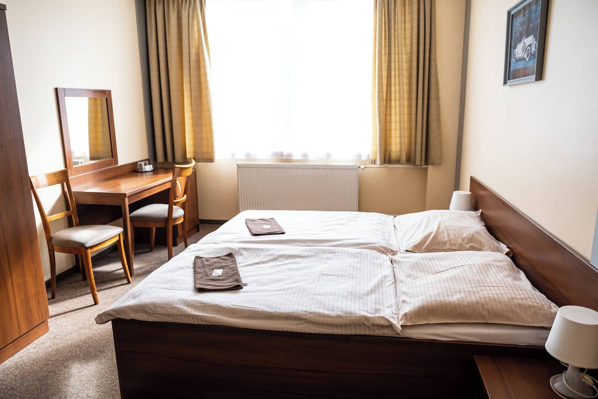 A hotel room with a bed, two chairs, a desk, a mirror, and a window with curtains.