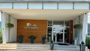 City-hotellin sisäänkäynti, jossa on puinen julkisivu, lasiovet ja ruukuissa olevia kasveja.