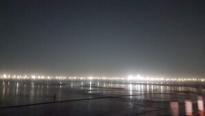 A nighttime view of a waterfront with a row of illuminated buildings. - Kumbh Luxury Tents (Prayagraj)