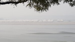 A foggy waterfront with a row of white buildings, likely a marina or dock area. - Kumbh Luxury Tents (Prayagraj)