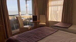 Quarto de hotel com duas camas, um laptop numa mesinha, uma cadeira e vista para o mar.