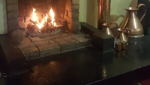Uma lareira com lenha acesa, uma chaleira de metal e uma panela de cobre tradicional em uma bancada preta.