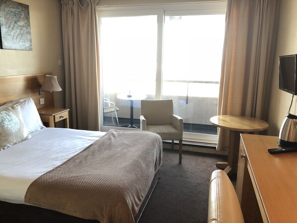 A hotel room with a bed, a desk, a chair, a small table, a TV, and a balcony with a chair and table. - Hotel Rosslare (Rosslare Harbour)