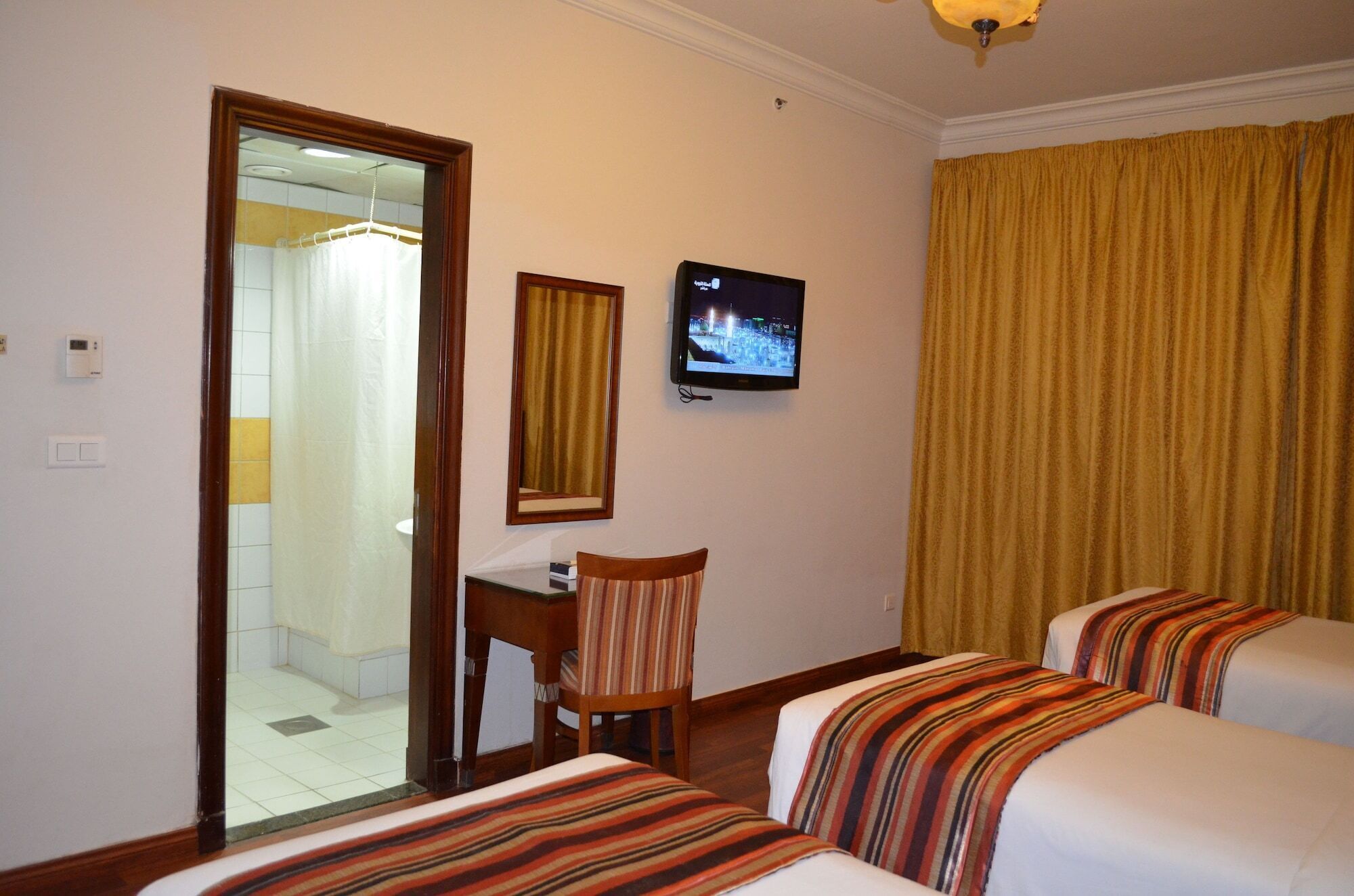 Habitación de hotel con cama, una silla, escritorio, televisión y baño visible a través de una puerta abierta.