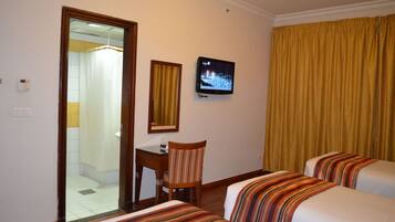 Habitación de hotel con cama, una silla, escritorio, televisión y baño visible a través de una puerta abierta.