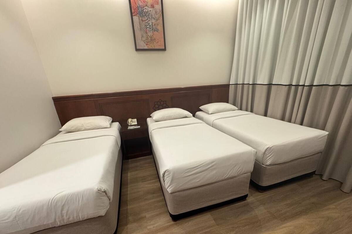 A hotel room with two single beds and a double bed, wooden flooring, a telephone on the nightstand, and a painting on the wall.