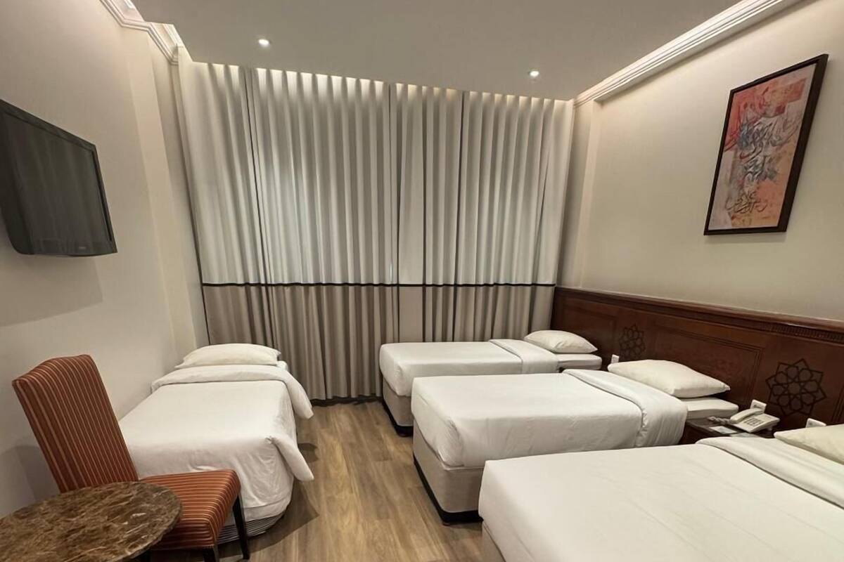 A hotel room with four beds, a small table, a chair, and a TV mounted on the wall.