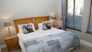 A double bed with a patterned bedspread, two decorative pillows, a wooden headboard, bedside tables with lamps, and a window with blinds. - Villa 14 (Knysna)