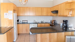 A kitchen with wooden cabinets, a black countertop, a built-in oven, a coffee maker, and a kettle. - Villa 14 (Knysna)