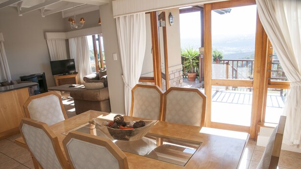 A dining area with a wooden table and chairs, a bowl of fruit, and a television in the background. - Villa 14 (Knysna)