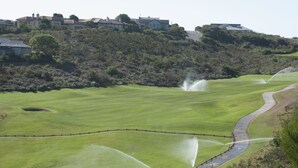 A golf course with a water sprinkler system, a curved road, and houses in the background. - Villa 14 (Knysna)