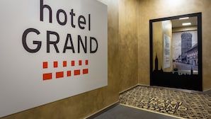 A hallway with a sign reading "hotel GRAND" and a mirrored wall reflecting a building facade. - Hotel GRAND (Caslav)