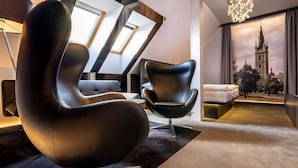 A modern living room with a unique black chair, a sofa, and a large window with skylight. - Hotel GRAND (Caslav)