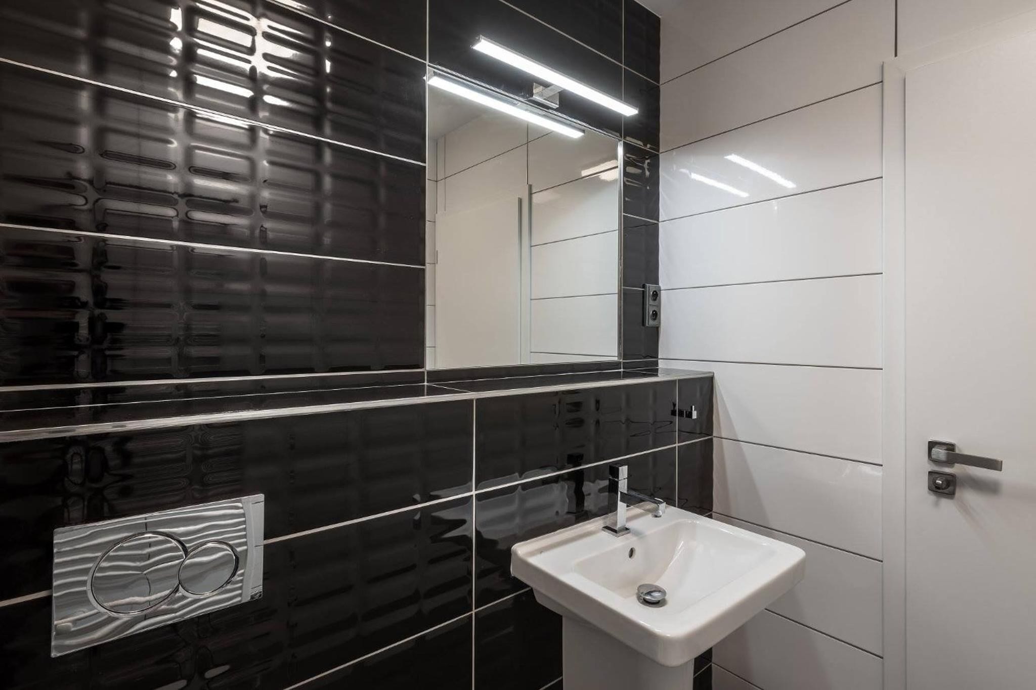Une salle de bain moderne avec des murs carrelés en noir et blanc, un lavabo blanc et un miroir.