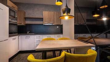 Una cocina moderna con armarios blancos, horno integrado y zona de comedor con mesa de madera y sillas amarillas.