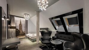 A modern hotel room with a large bed, a seating area with a sofa and chairs, a small table, and a large window with a cityscape view. - Hotel GRAND (Caslav)