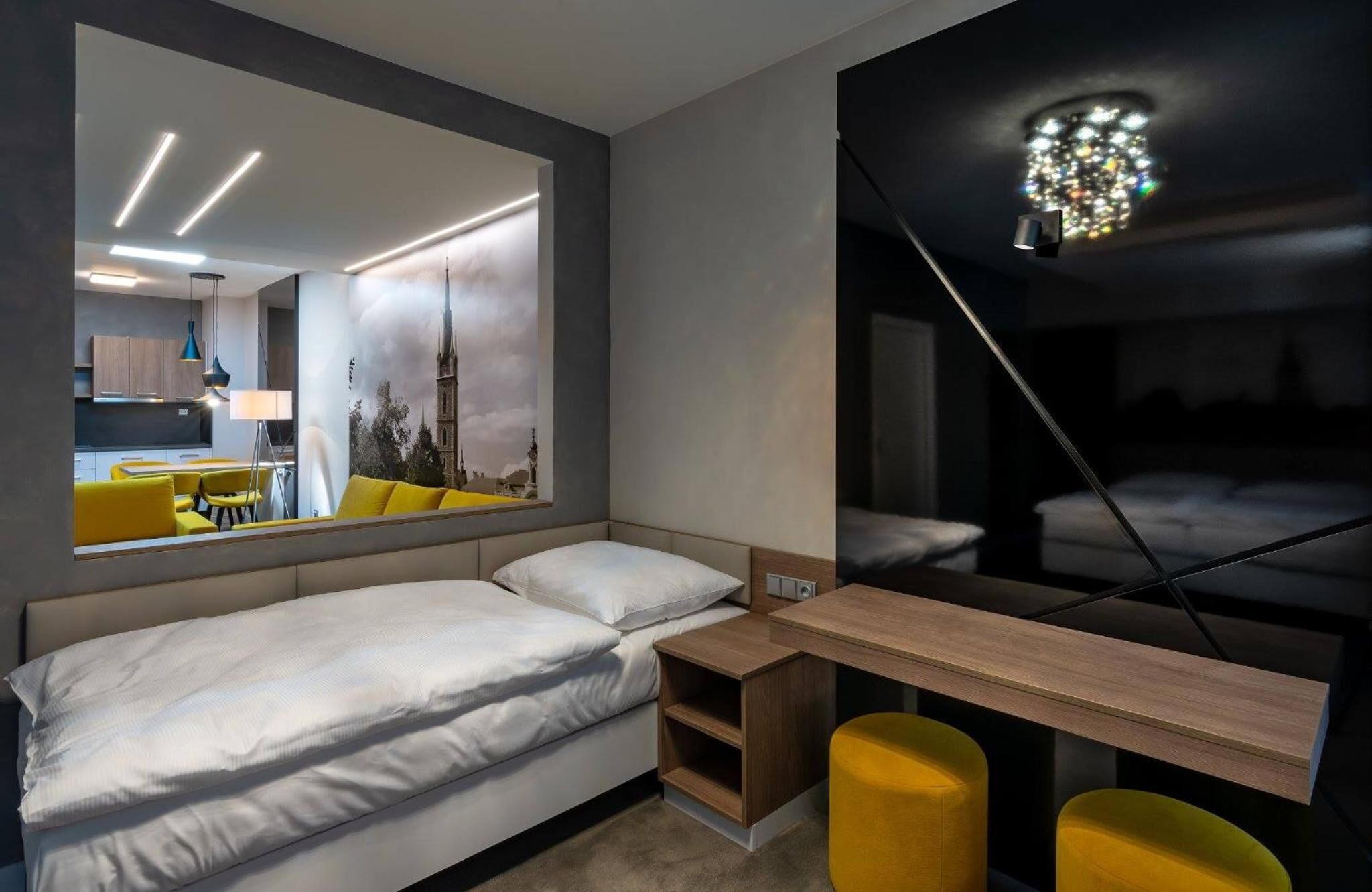 Habitació d'hotel moderna amb un mirall gran, un llit amb roba blanca, una petita taula de nit de fusta i un escriptori amb una cadira.