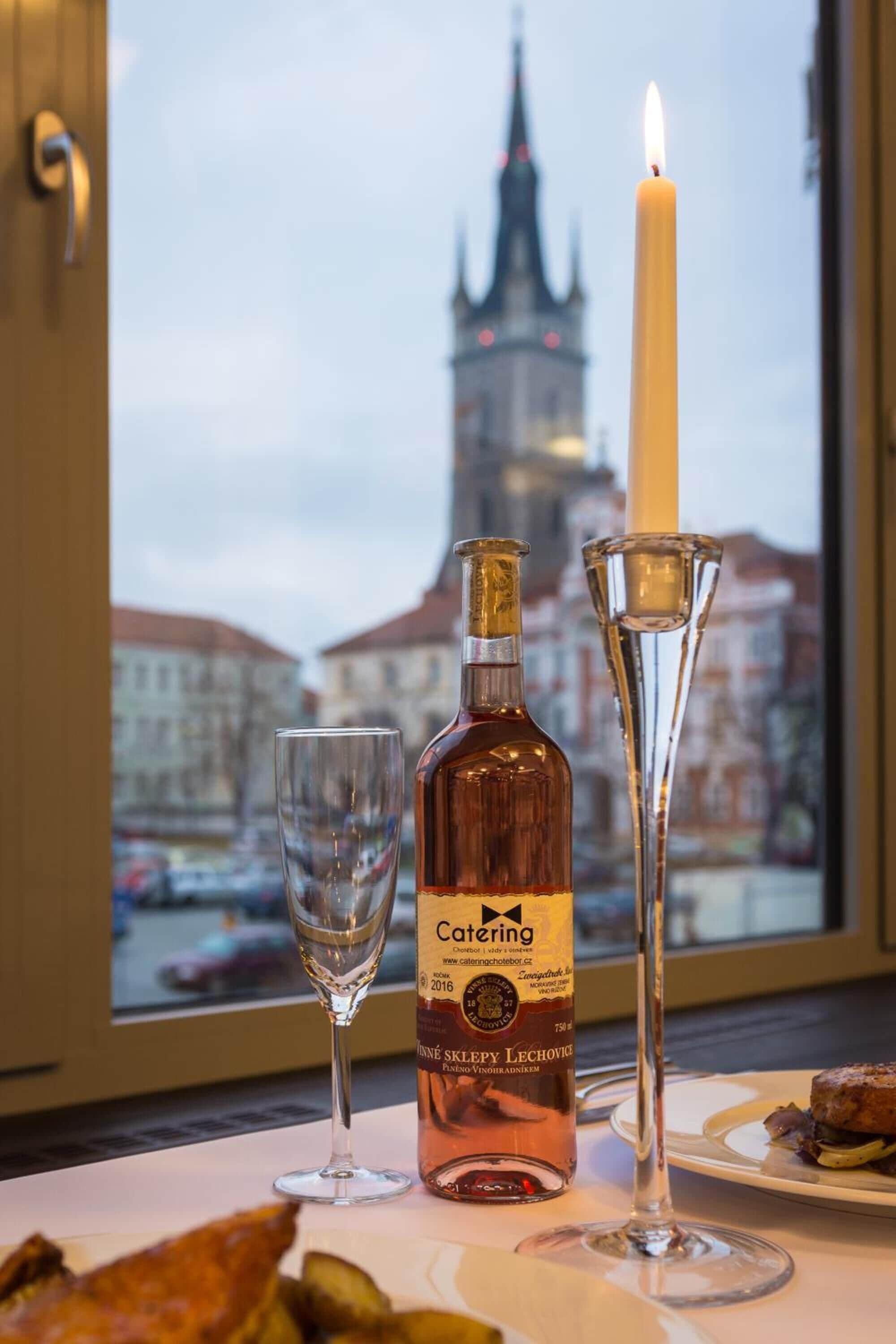 A bottle of Caterling wine, a candle, and a glass on a table with a view of a cityscape and a tower in the background.