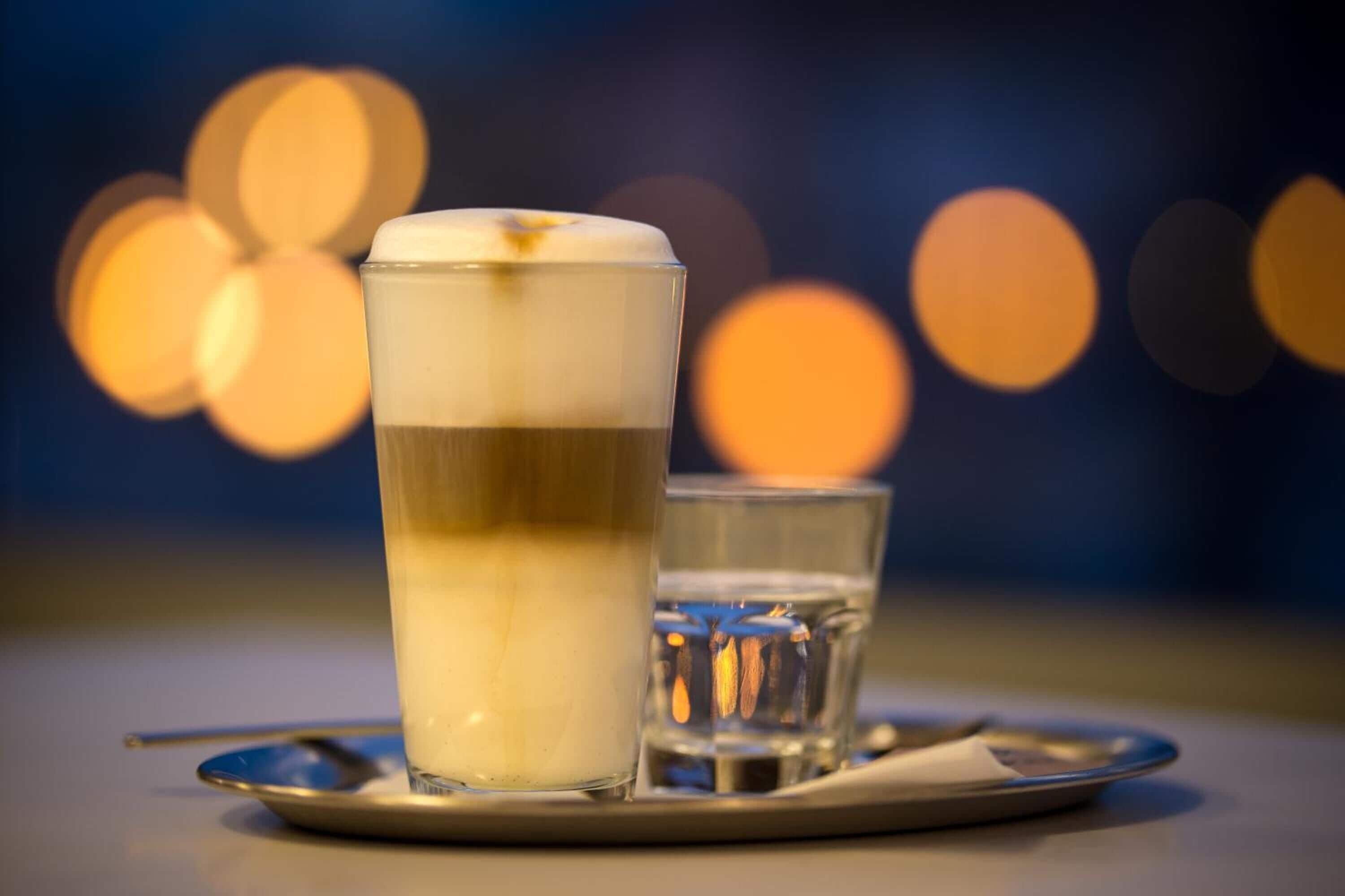 A tall glass with a layered drink, a smaller glass, and a spoon on a tray.