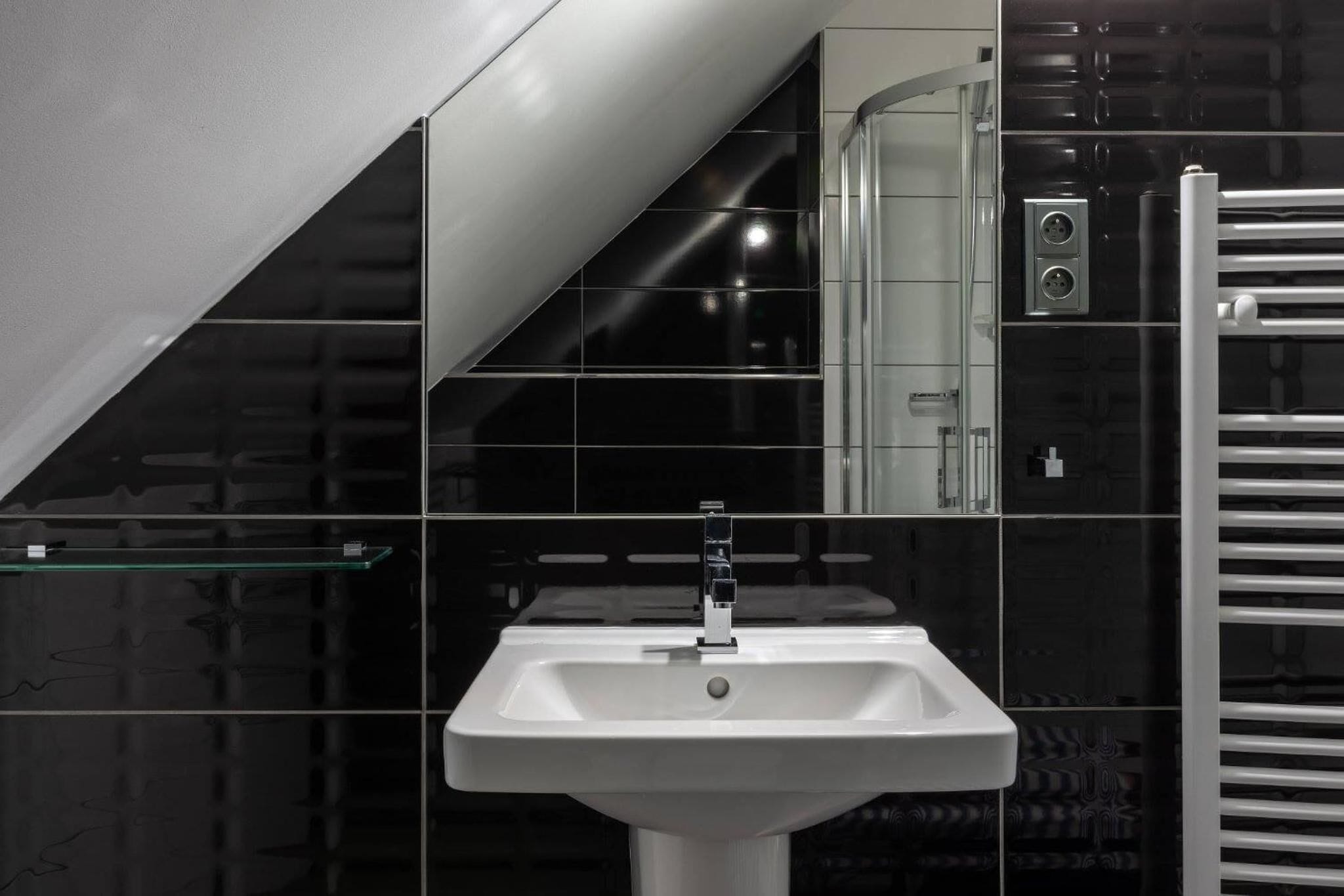 A modern bathroom with a white sink, black tiled walls, and a glass shelf.