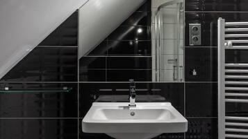 A modern bathroom with a white sink, black tiled walls, and a glass shelf.
