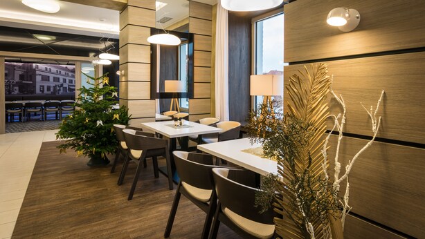 A modern dining area with wooden paneling, a Christmas tree, and a large window. - Hotel GRAND (Caslav)