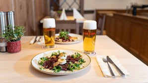 A dining table with plates of food, two glasses of beer, and cutlery.