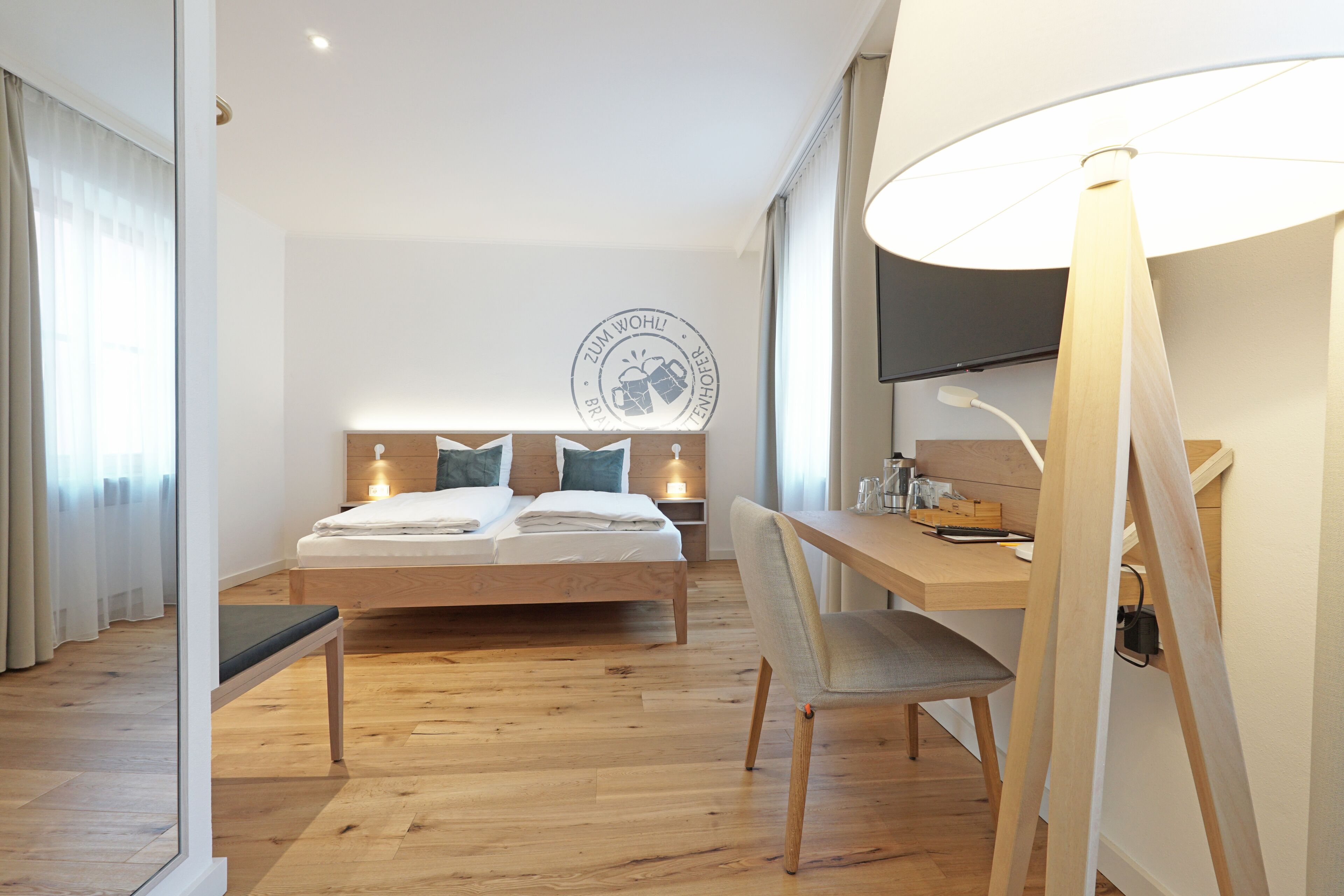 A modern hotel room with a wooden bed, a desk, and a large window.