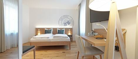 A modern hotel room with a wooden bed, a desk, and a large window.