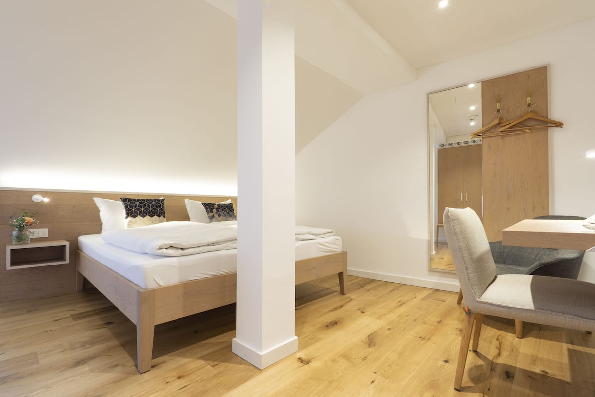 A modern bedroom with two beds, a wooden desk, and a large mirror.