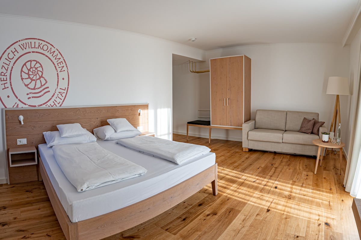 A hotel room with a wooden bed, a sofa, a wardrobe, and a lamp.