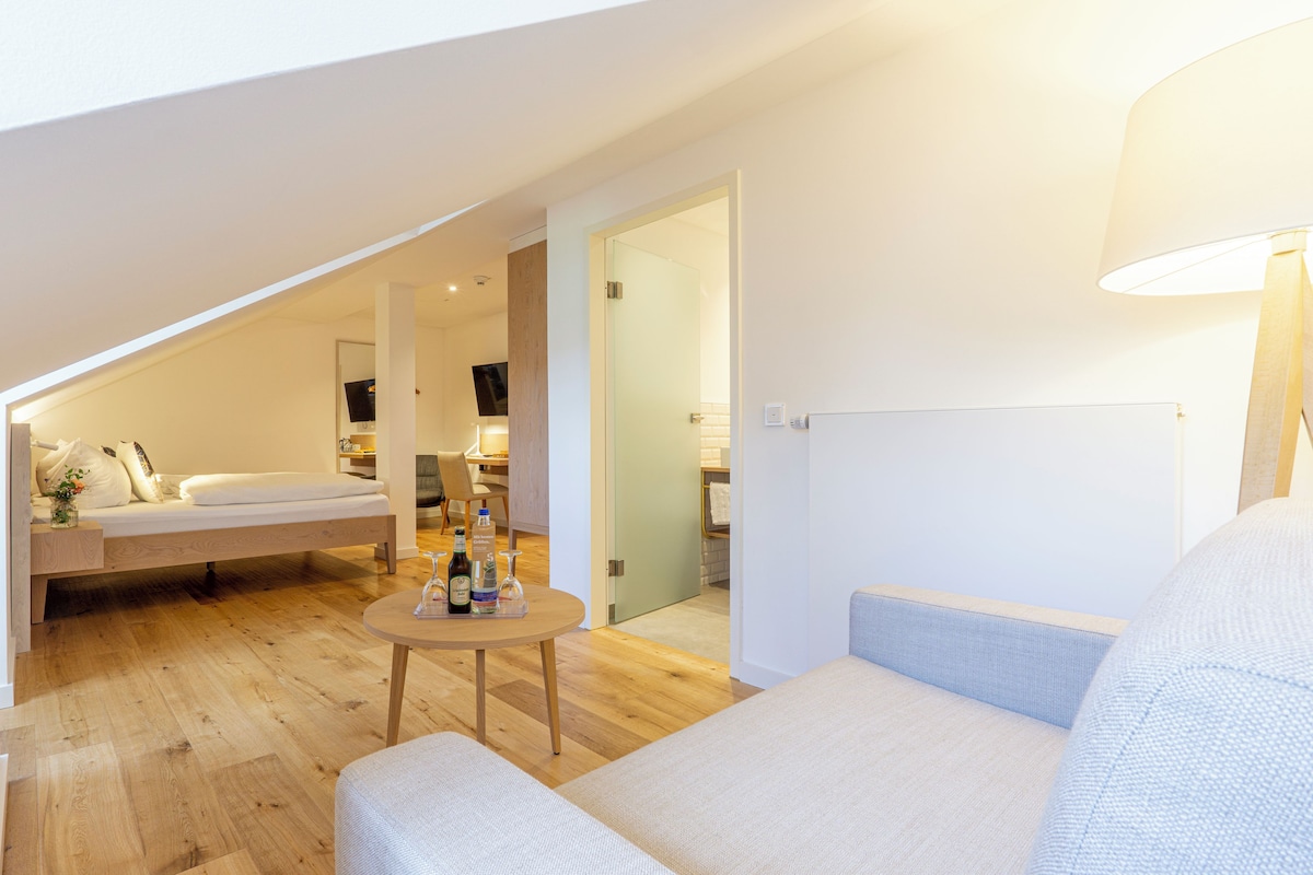 A modern loft bedroom with a loft bed, a small table with bottles, and a sofa.