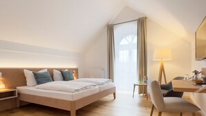 A hotel room with a bed, bedside table, lamp, chair, and a desk with a mirror.