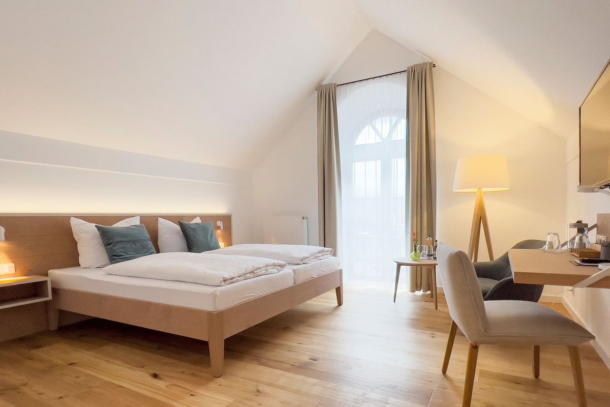 A hotel room with a bed, bedside table, lamp, chair, and a desk with a mirror.