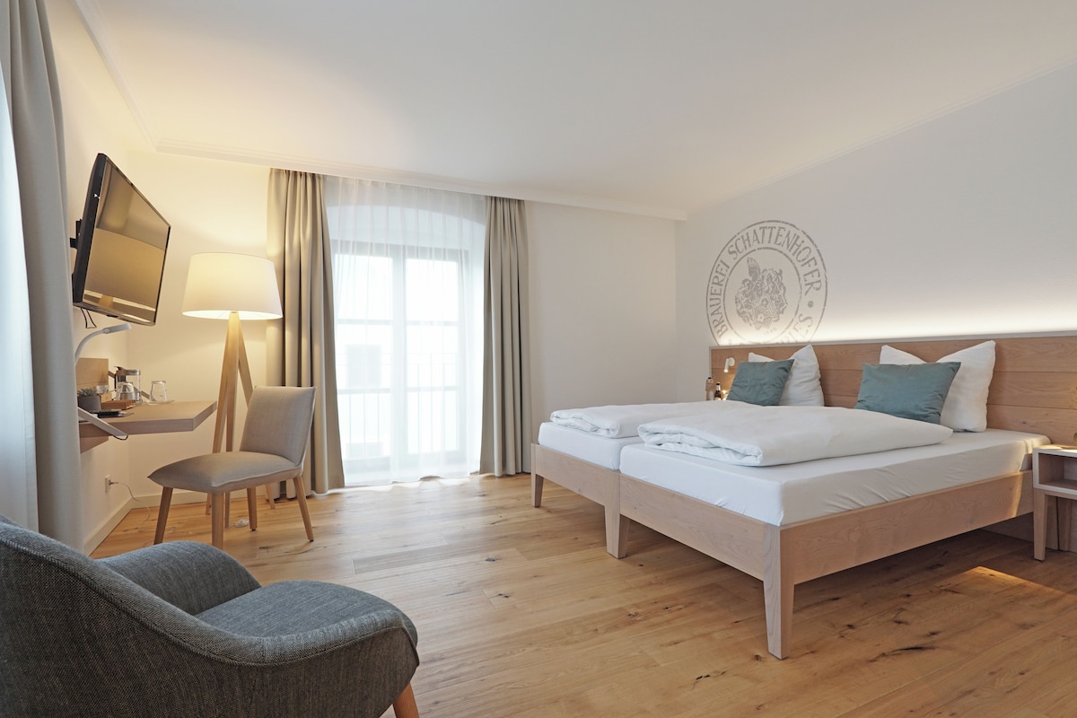 A hotel room with a wooden bed, a desk with a chair, a television, and a large window with curtains.