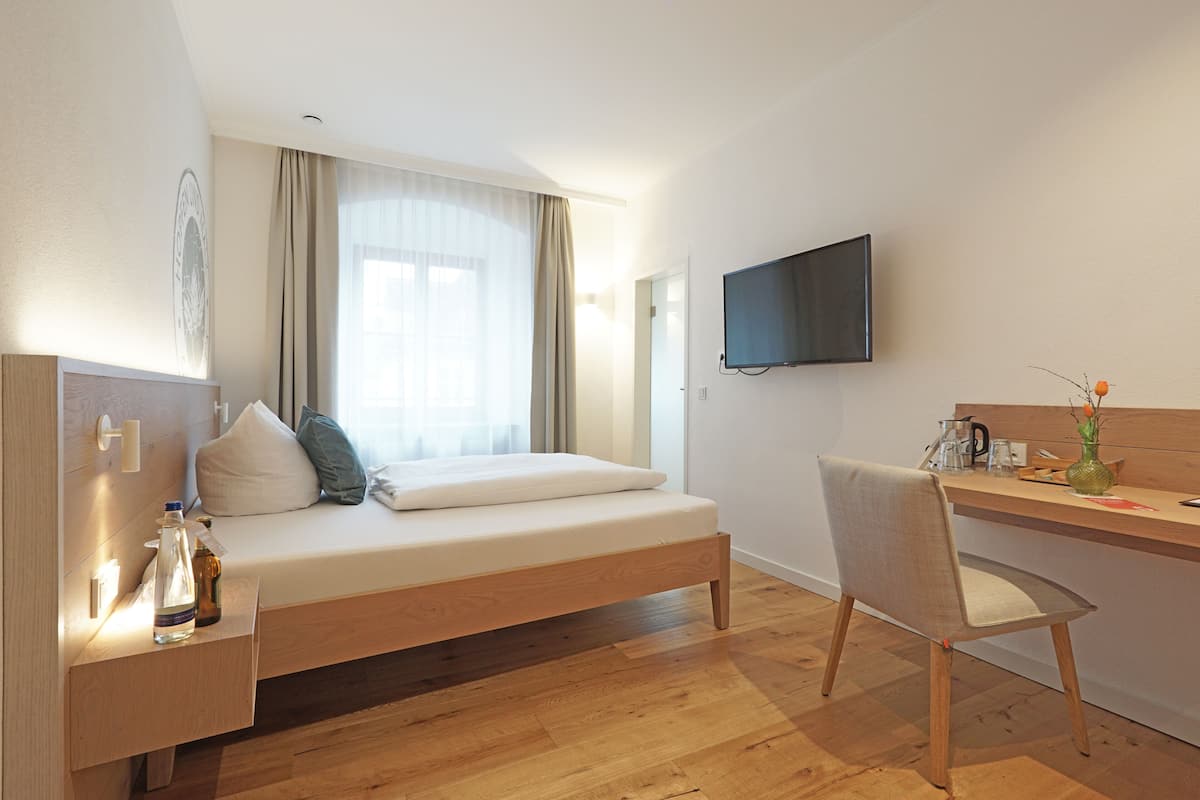 A modern hotel room with a wooden bed, a desk, and a TV mounted on the wall.