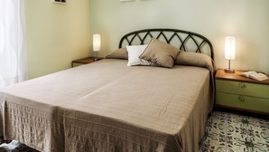 Un lit bien fait, recouvert d’une courtepointe matelassée, avec deux lampes de chevet et une table de chevet verte dotée d’un tiroir.