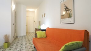 Un couloir avec un canapé, une affiche encadrée et un vase vert.