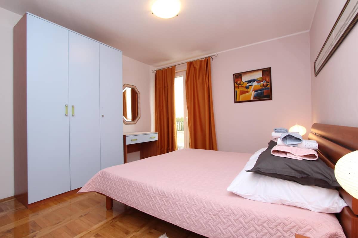 Quarto com cama, guarda-roupa, escrivaninha e janela com cortinas.