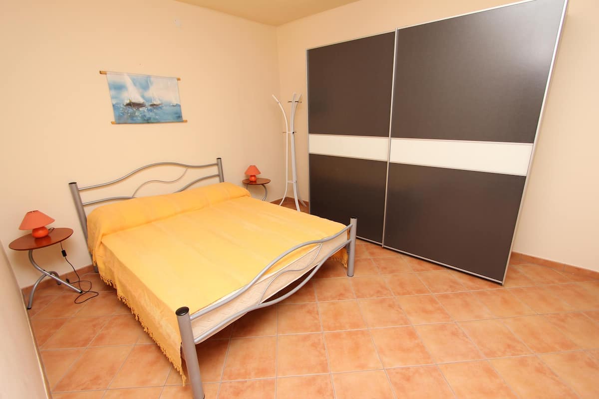 Quarto com cama, mesa de cabeceira, luminária, pintura e guarda-roupa.