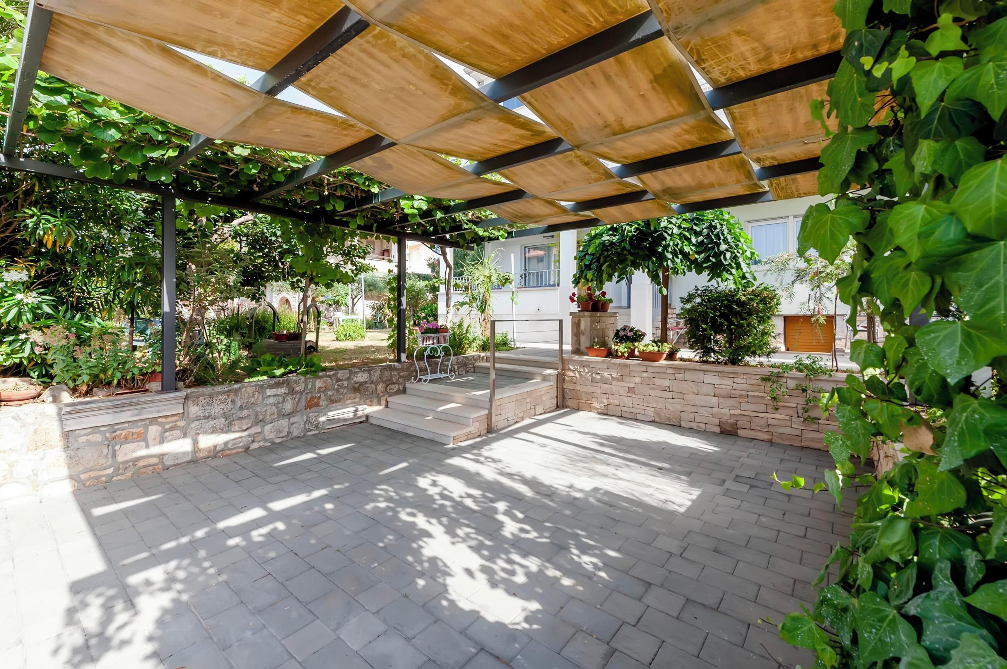 Een terras buiten, met een pergola, stenen muren en potplanten.